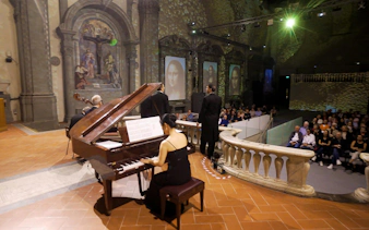 Pianist and tenors performing at a concert in Florence with an audience in a historic venue.