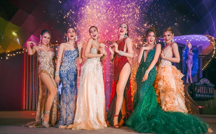 Performers in vibrant costumes at Simon Cabaret Show, Phuket, with fireworks in the background.