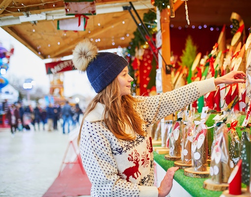Woman browsing festive stalls at a Christmas market in Paris during winter.