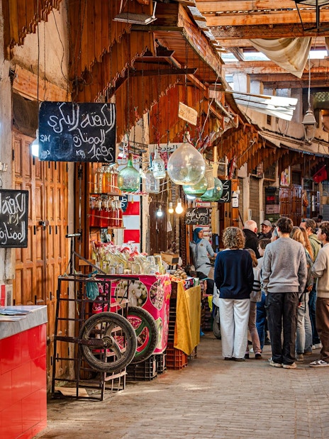Visitors exploring vibrant stalls in Marrakech Souks, Morocco.