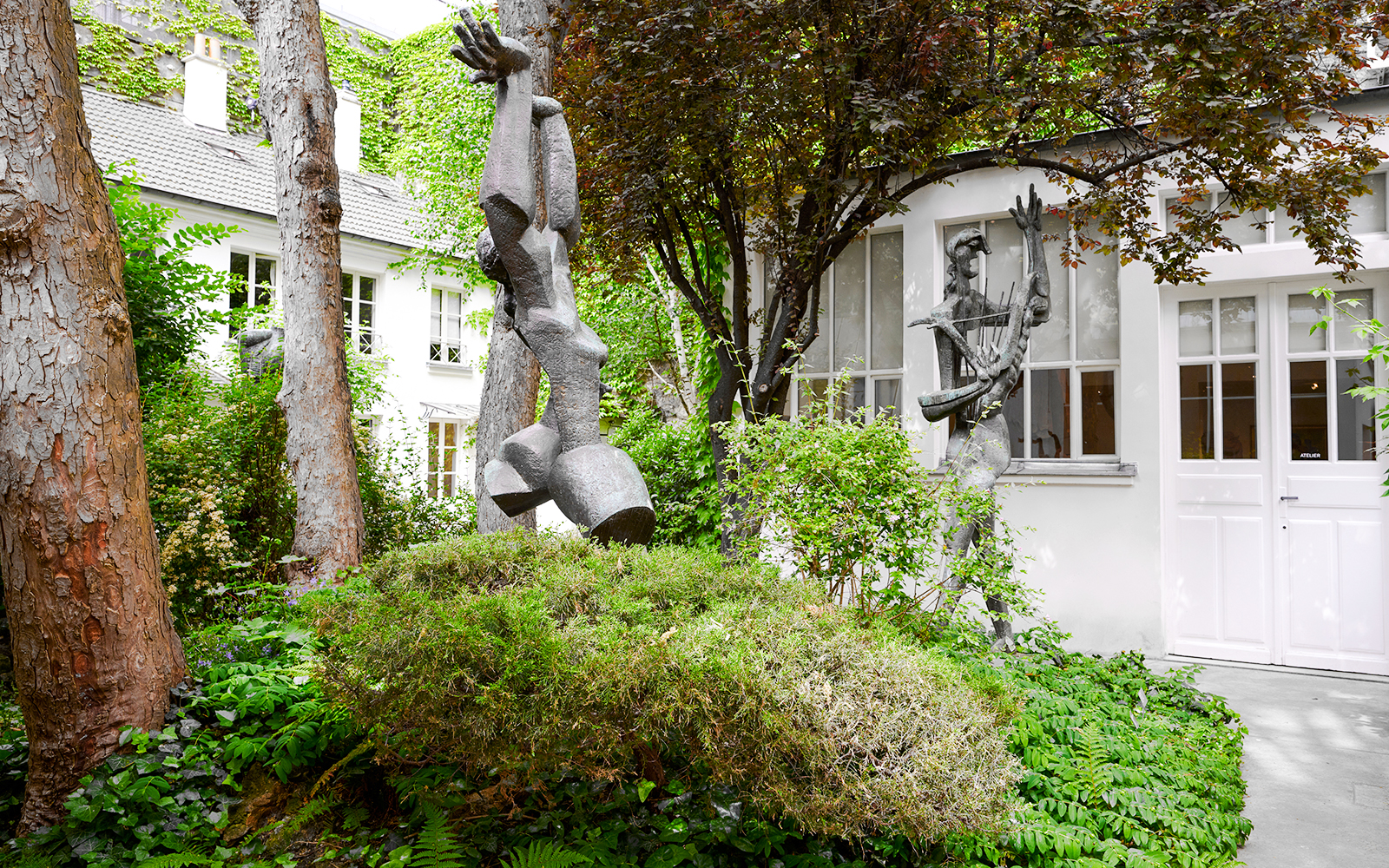Sculptures in the garden of Zadkine Museum, Paris, surrounded by lush greenery.