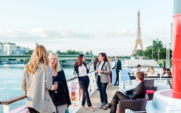 Guests enjoying a Paris Bastille Day dinner cruise with Eiffel Tower view.