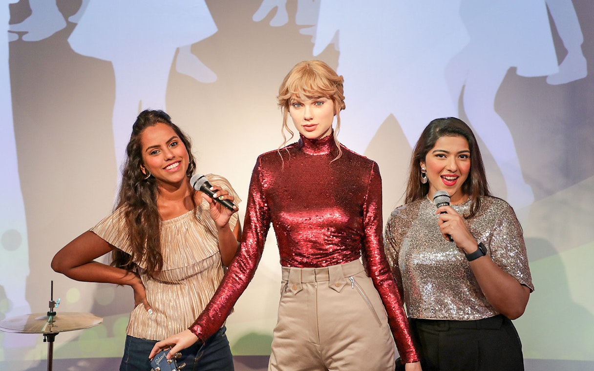 Wax figure with visitors holding microphones at Madame Tussauds Dubai.