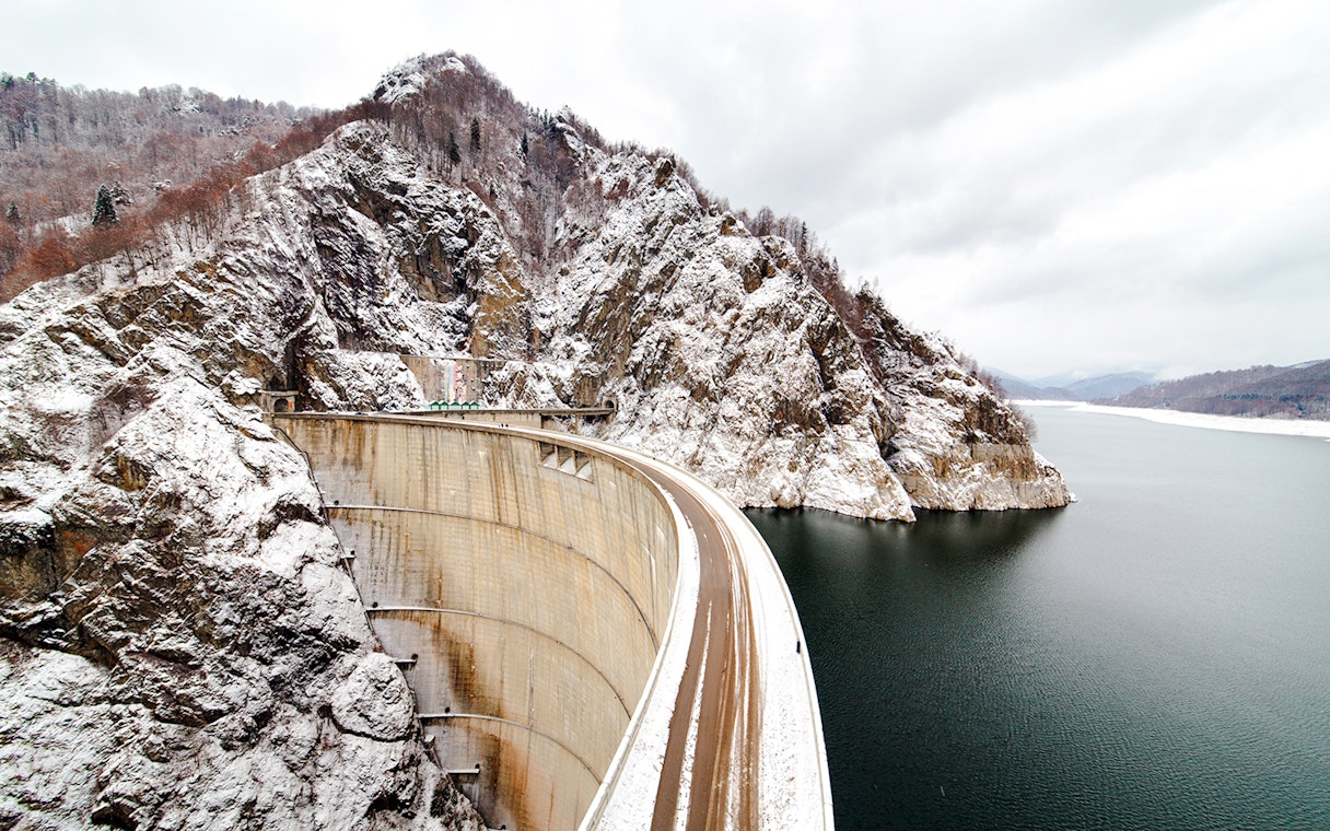 Vidraru Dam in Romania with snow-covered mountains and reservoir.