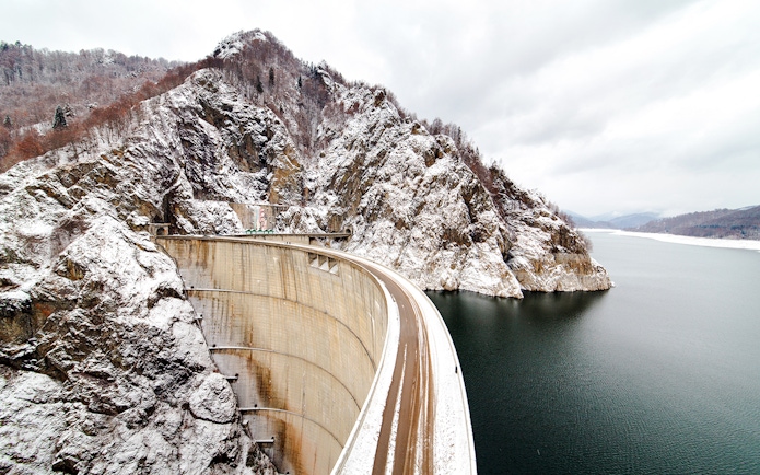 Vidraru Dam in Romania with snow-covered mountains and reservoir.