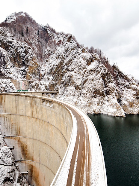 Vidraru Dam in Romania with snow-covered mountains and reservoir.