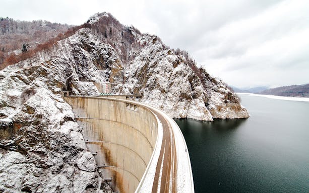 Vidraru Dam in Romania with snow-covered mountains and reservoir.