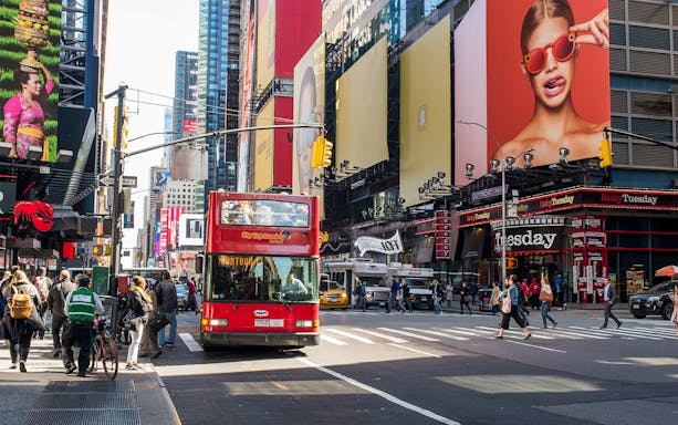 Red double-decker bus on a busy street in Times Square, New York, during a City Sightseeing tour.