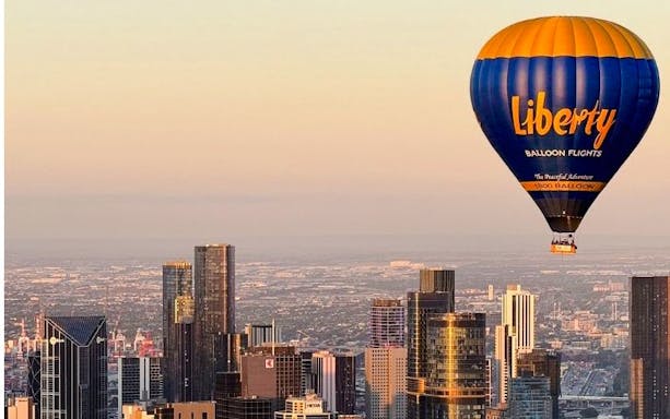Hot air balloon over Melbourne skyline at sunrise.