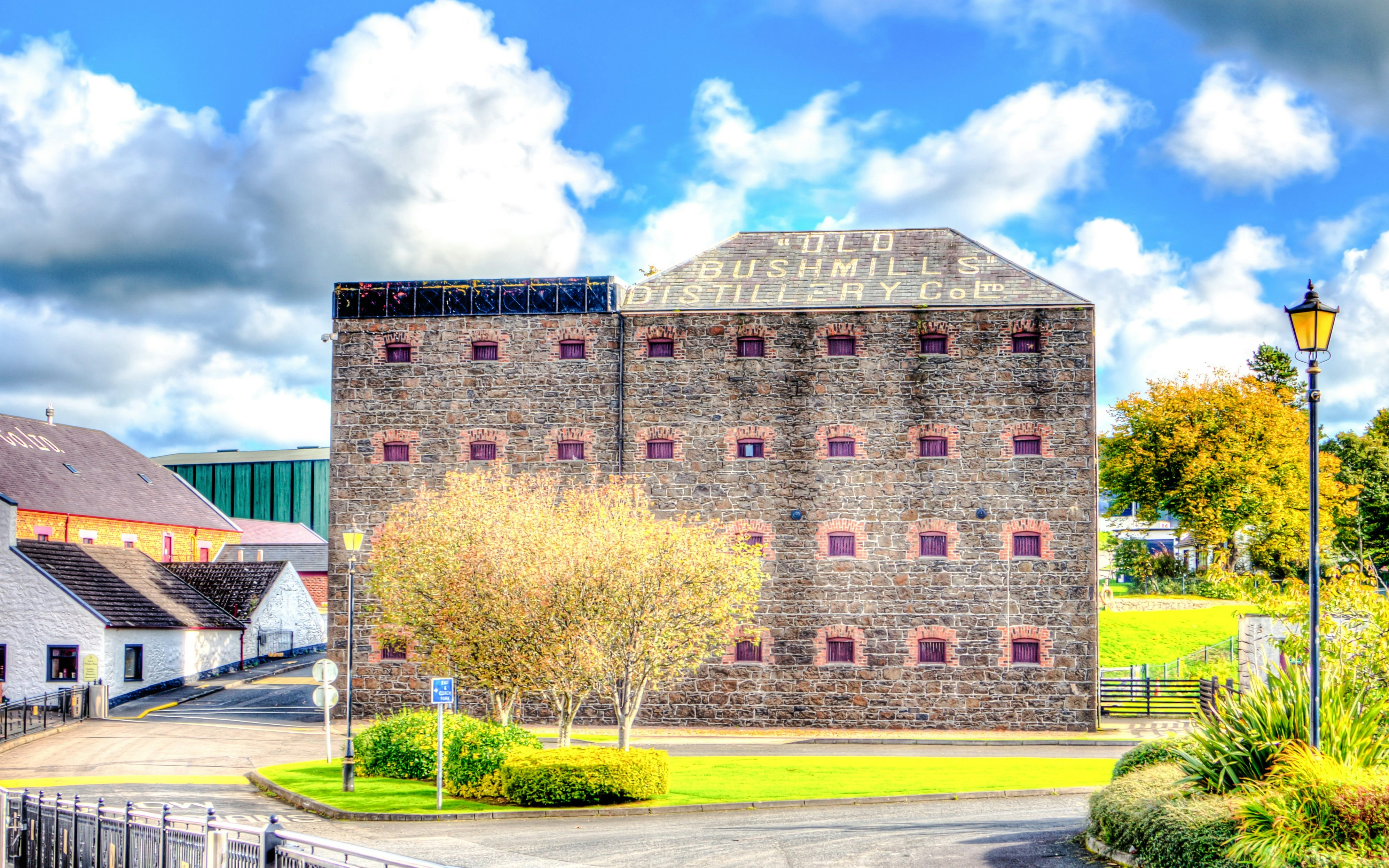 Old Bushmills Distillery stone building with trees and lamppost in foreground.