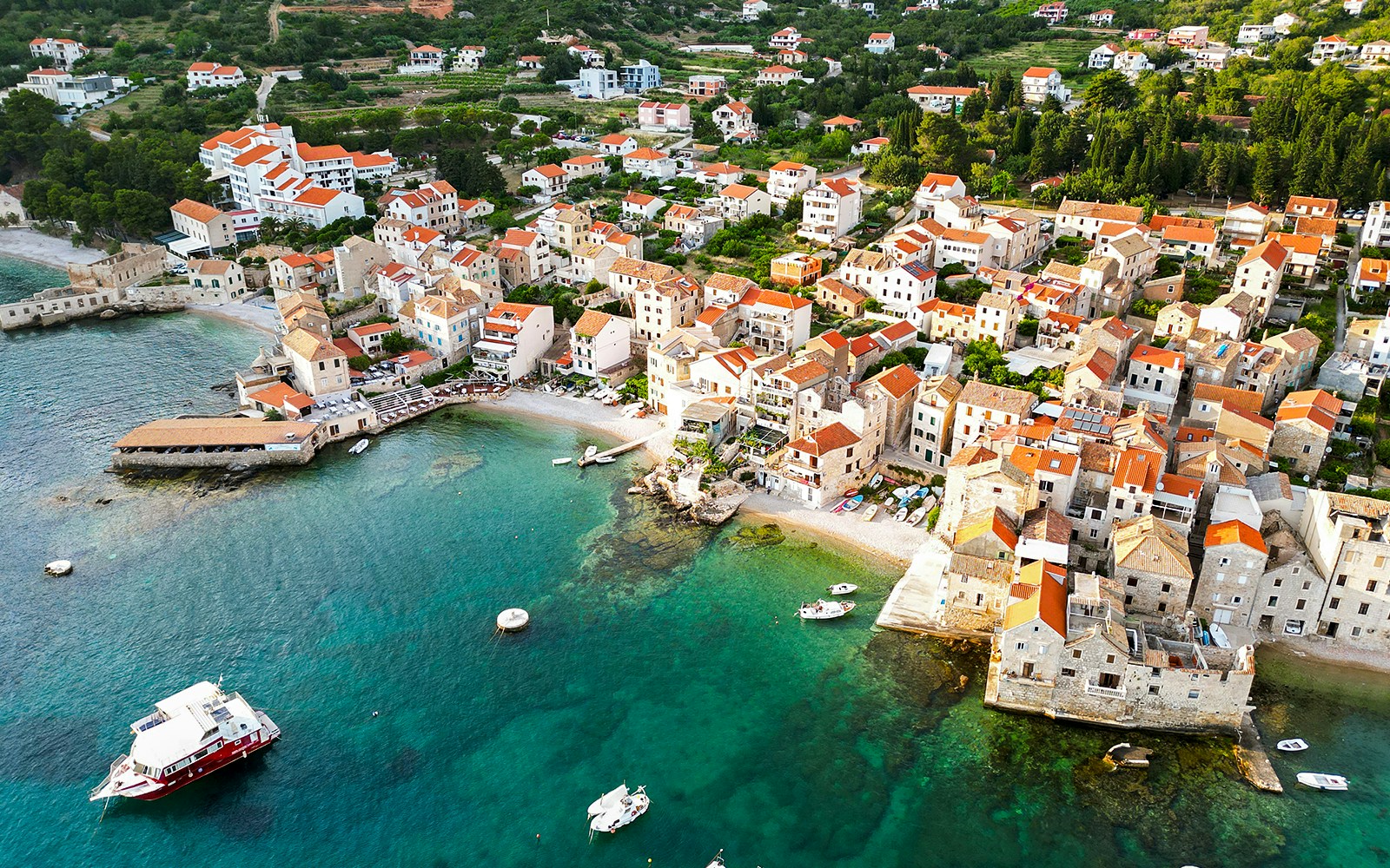 Aerial view of Komiza town with red-roofed buildings and boats in Vis, Croatia.