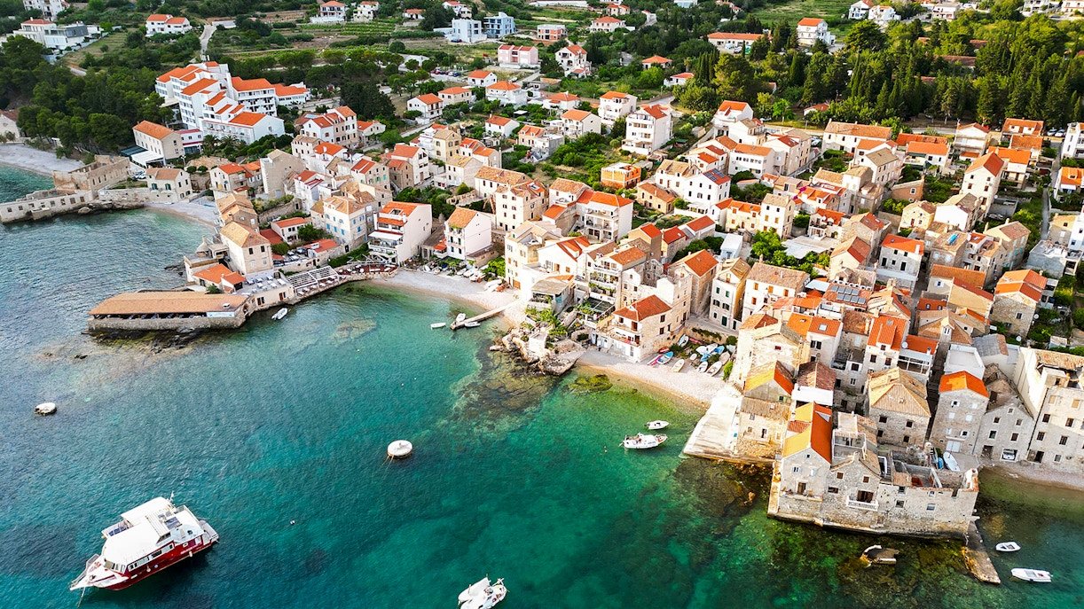 Aerial view of Komiza town with red-roofed buildings and boats in Vis, Croatia.