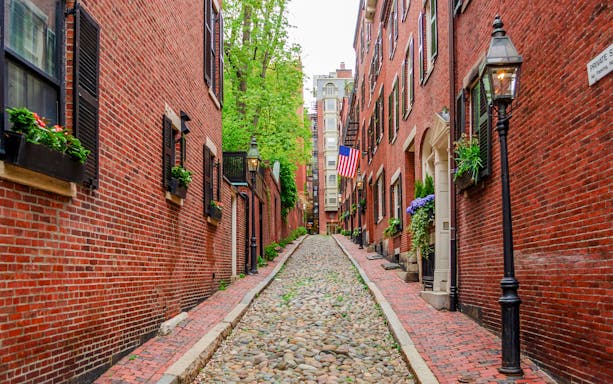 Cobblestone street in Boston's historic Beacon Hill neighborhood with brick buildings and American flag.