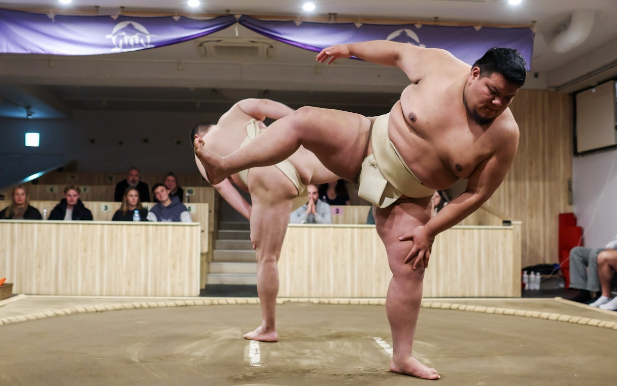 Sumo wrestlers performing in a Tokyo arena with spectators watching.