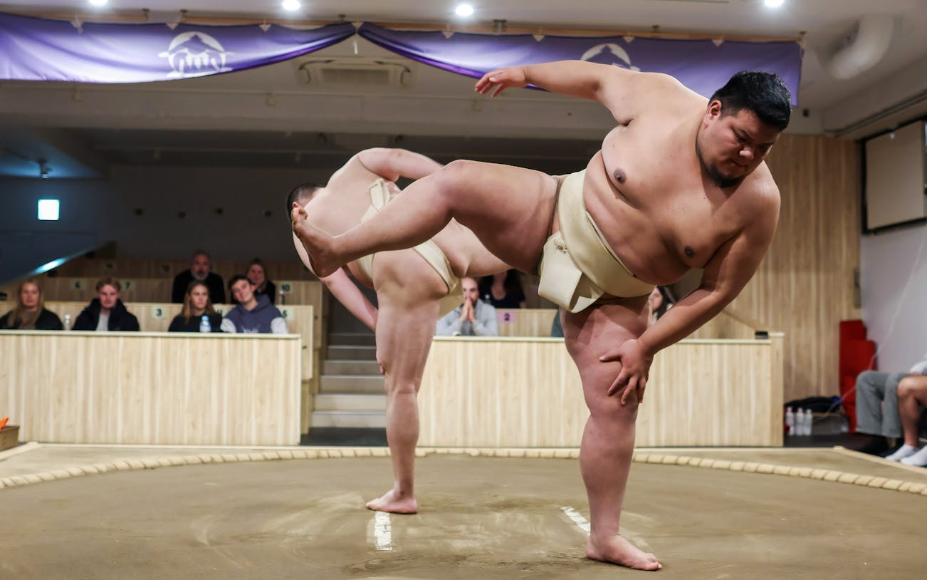 Sumo wrestlers performing in a Tokyo arena with spectators watching.