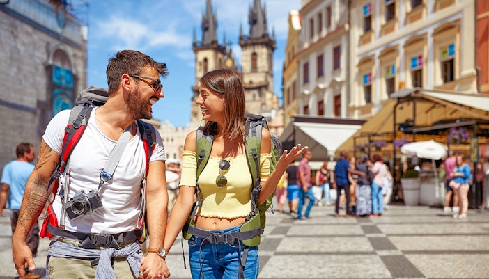 Tourist couple exploring Old Town Square, Prague with Tyn Church in background.