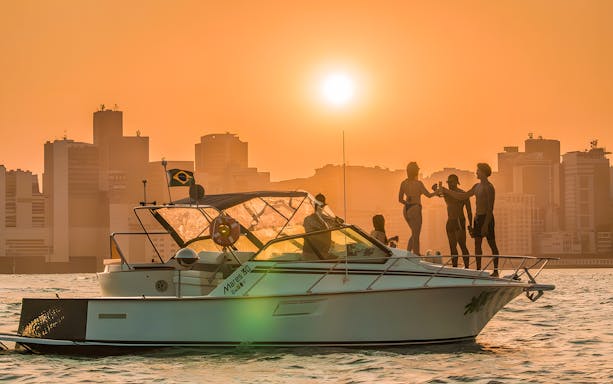 Tourists enjoying a sunset cruise in Rio de Janeiro with city skyline in the background.