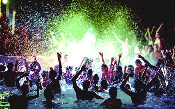People celebrating at a vibrant pool party with colorful lights and splashing water.