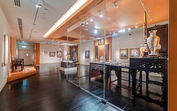 Peranakan Museum gallery with traditional artifacts and portraits on display.