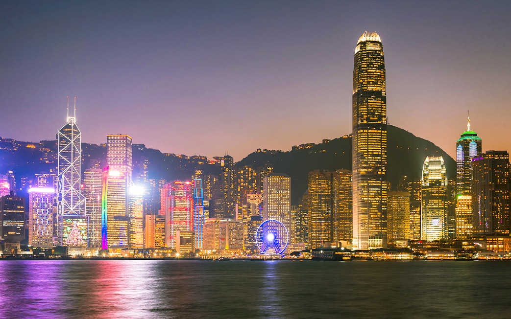 Hong Kong skyline at night with illuminated skyscrapers and Ferris wheel.