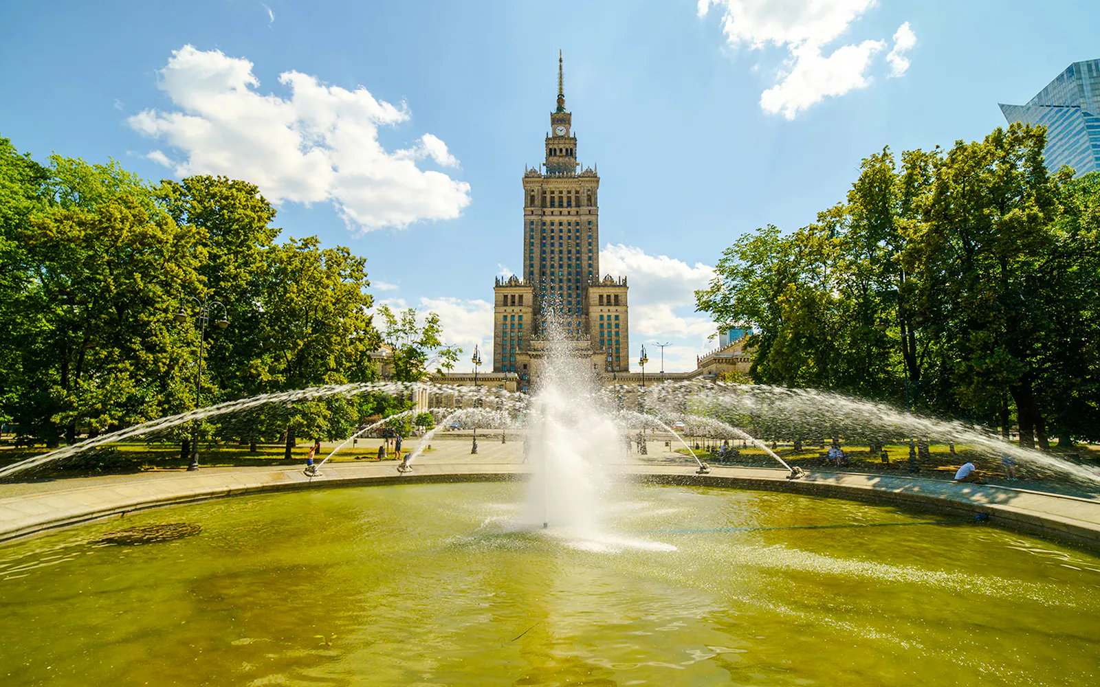 Fountain in front of the Palace of Culture and Science, Warsaw, surrounded by trees.