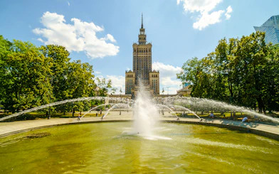 Fountain in front of the Palace of Culture and Science, Warsaw, surrounded by trees.