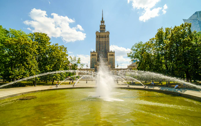 Fountain in front of the Palace of Culture and Science, Warsaw, surrounded by trees.