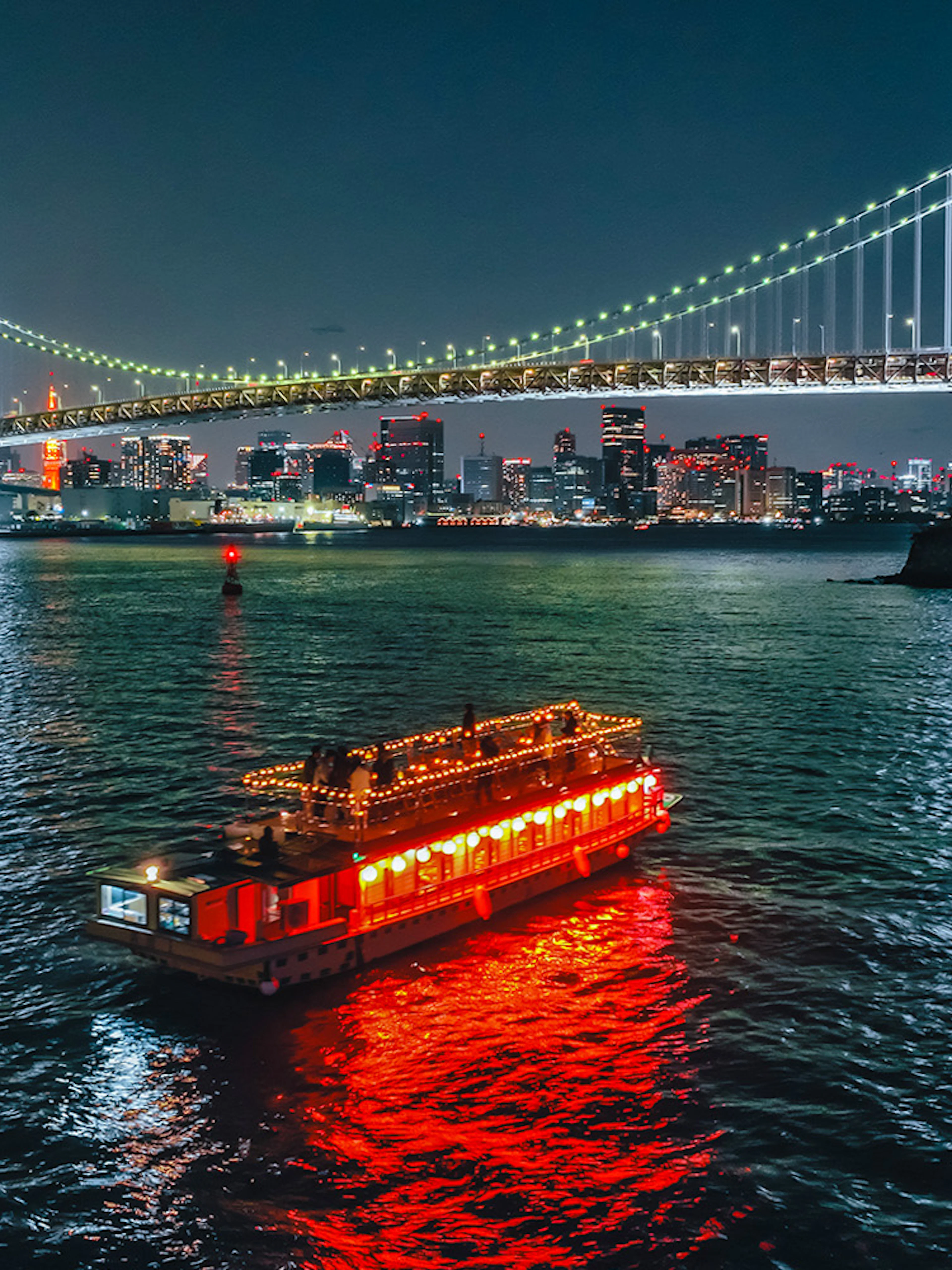 Yakatabune boat with lights on Tokyo Bay under Rainbow Bridge at night.
