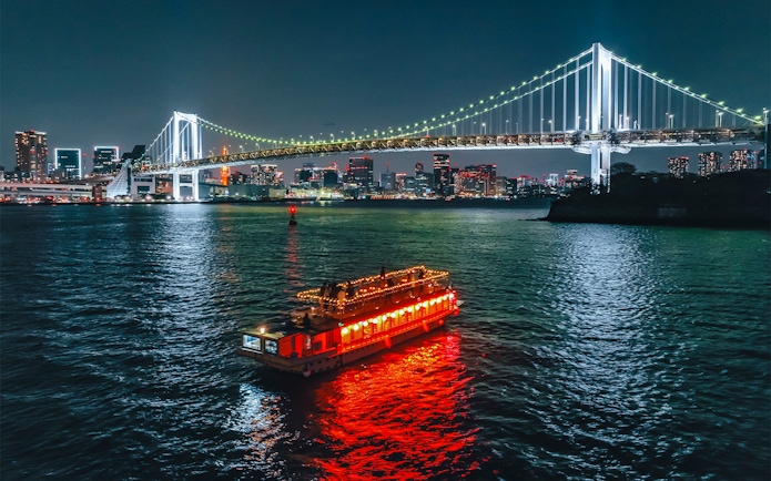 Yakatabune boat with lights on Tokyo Bay under Rainbow Bridge at night.