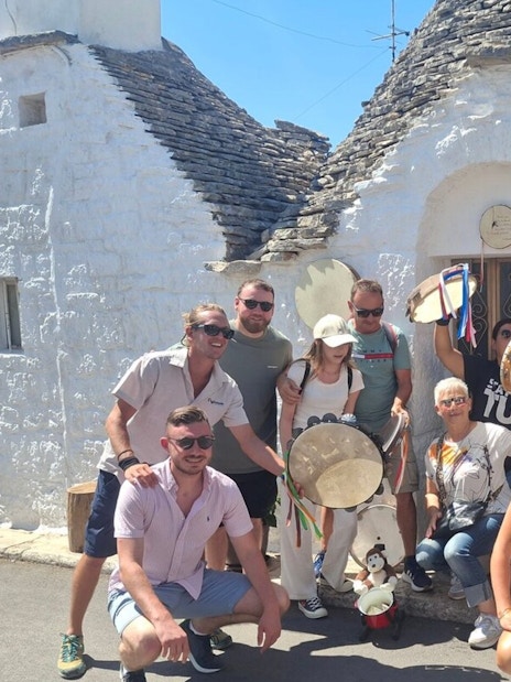 Tourists with tambourines in front of trulli houses in Alberobello, Italy.