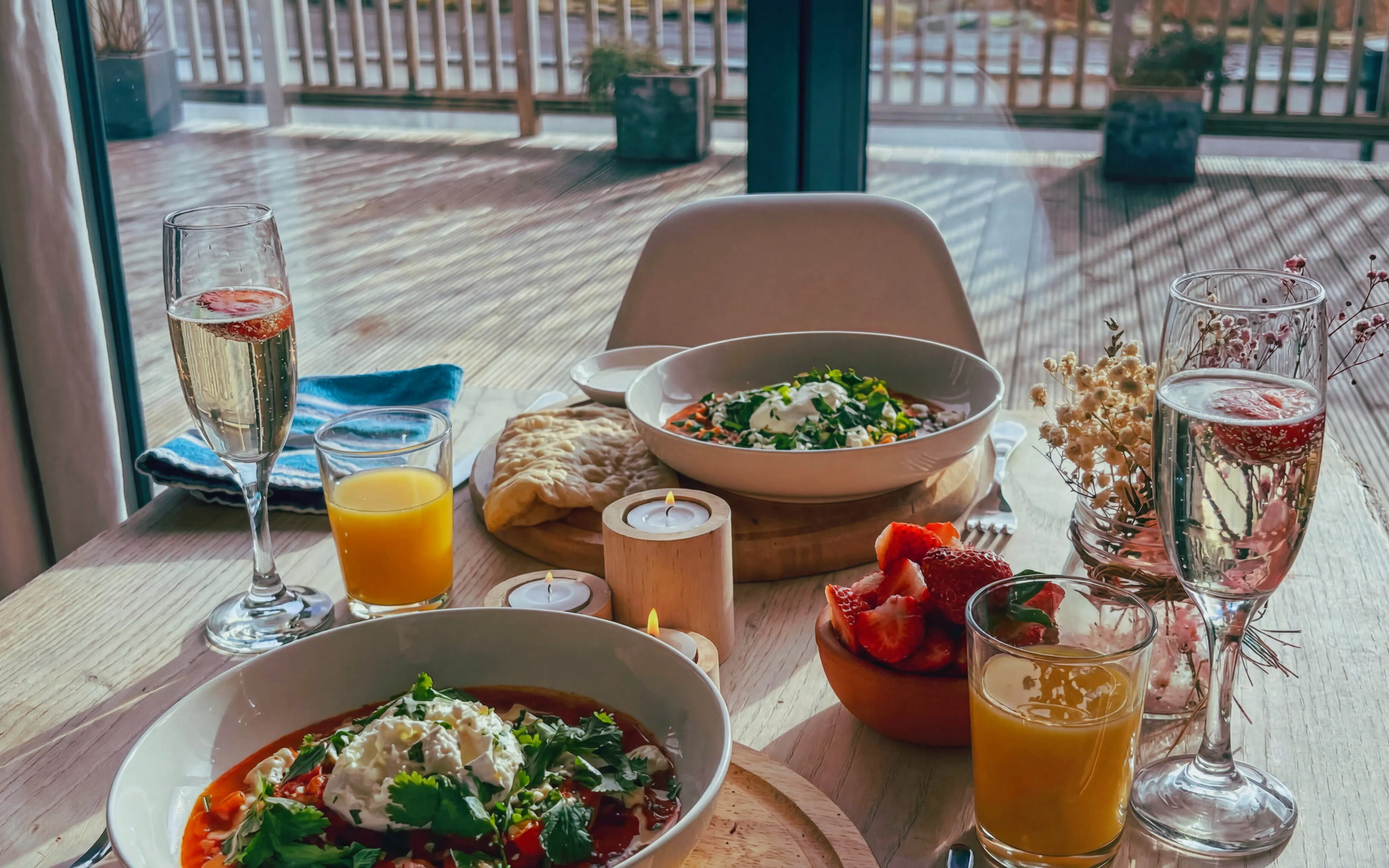 Hotel breakfast with fresh fruit, orange juice, and sparkling wine on a sunlit terrace.
