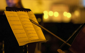 Sheet music and cello bow at candlelit Queen performance, Chopin Gallery, Krakow.
