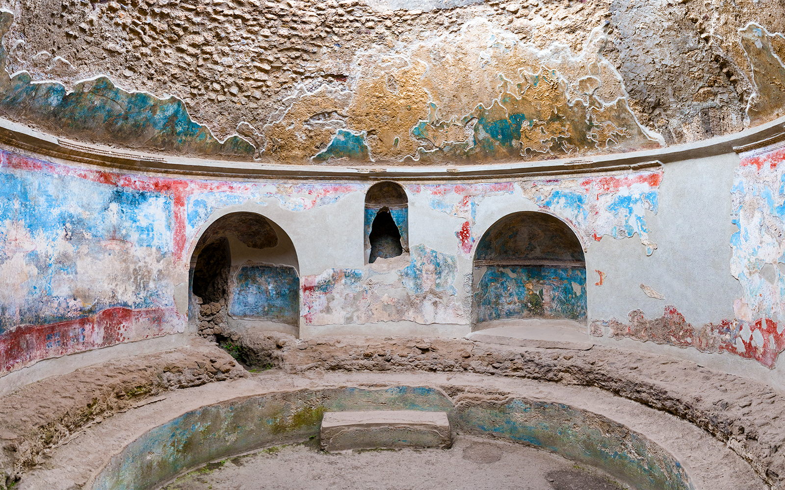 Pompeii Baths ancient frescoes and stone seating in circular room.