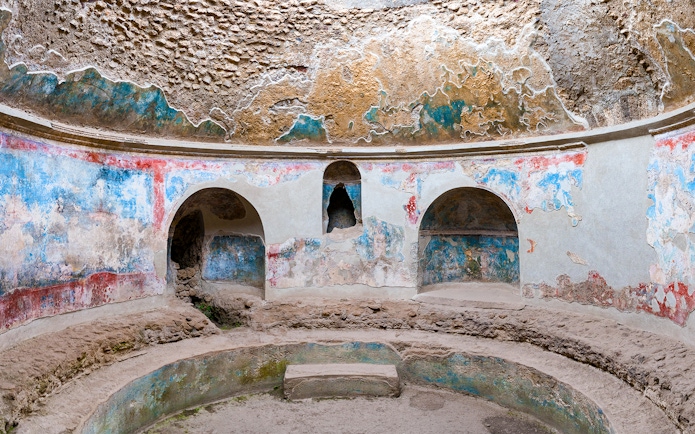 Pompeii Baths ancient frescoes and stone seating in circular room.
