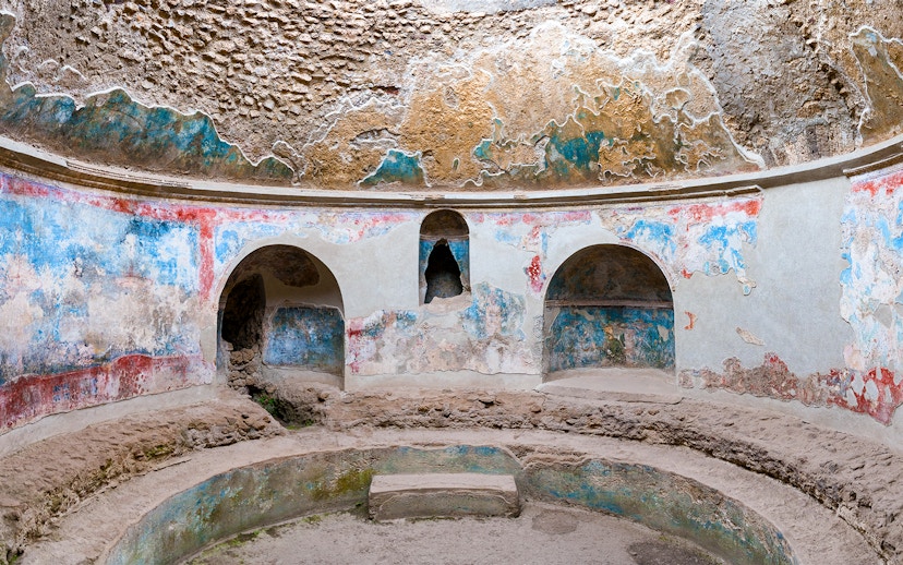 Pompeii Baths ancient frescoes and stone seating in circular room.