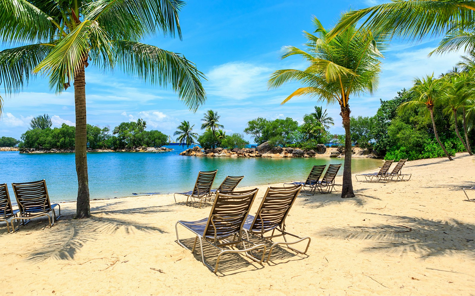 Sun loungers on a sandy beach with palm trees at Sentosa Island, Singapore.