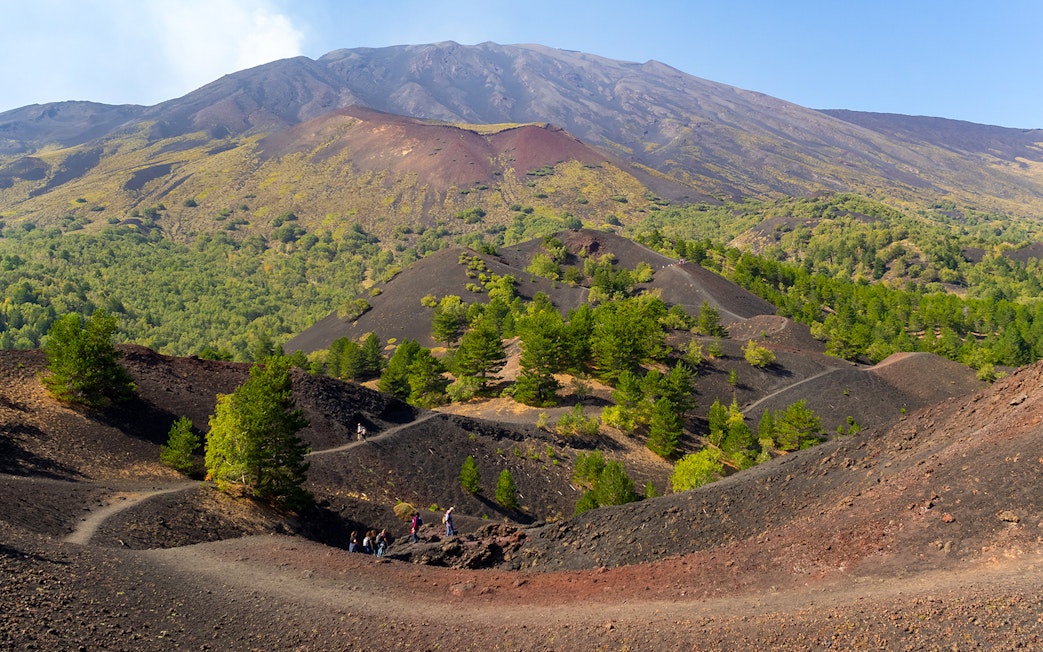 Mount Etna north slopes with side crater and hikers on volcanic terrain.