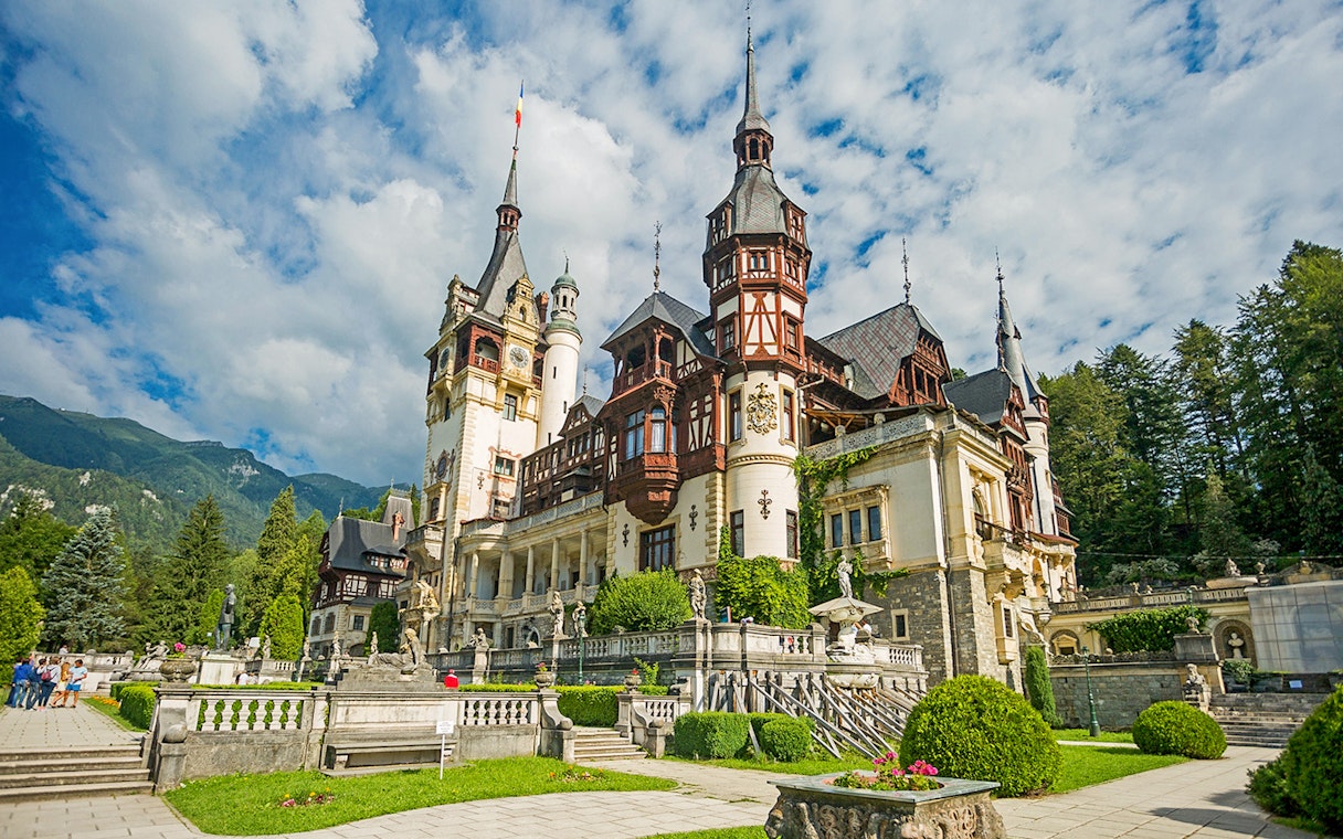 Peles Castle exterior with ornate towers and lush gardens in Sinaia, Romania.