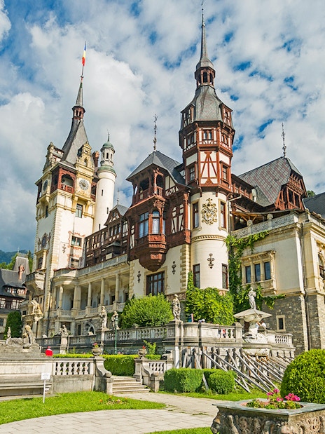 Peles Castle exterior with ornate towers and lush gardens in Sinaia, Romania.