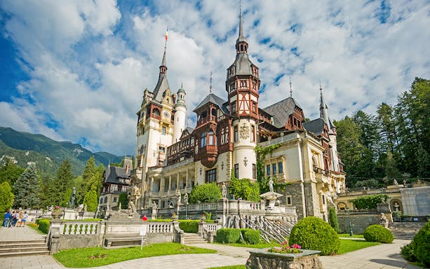 Peles Castle exterior with ornate towers and lush gardens in Sinaia, Romania.