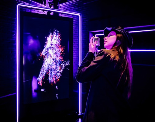 Person singing into a microphone with digital art display at Youseum Museum, Amsterdam.