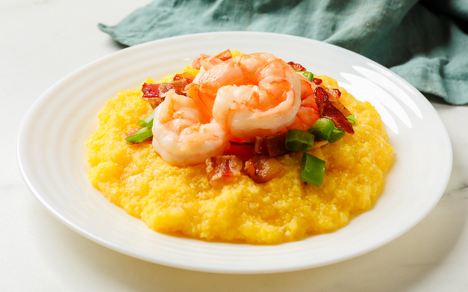 Shrimp and bacon on grits with green onion on a white plate.