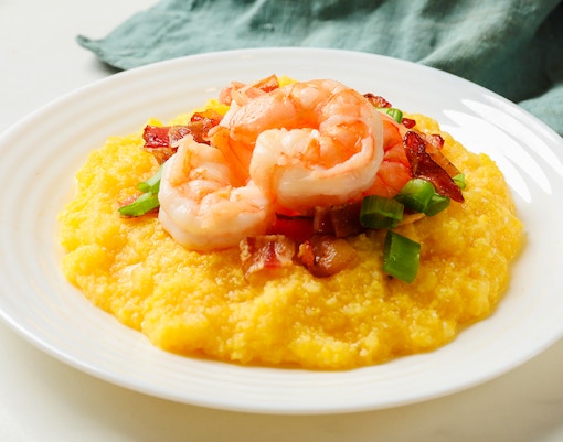 Shrimp and bacon on grits with green onion on a white plate.