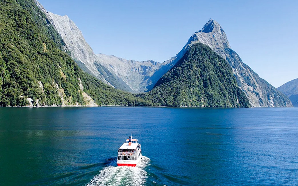 Cruise boat sailing through Milford Sound, New Zealand with mountain views.