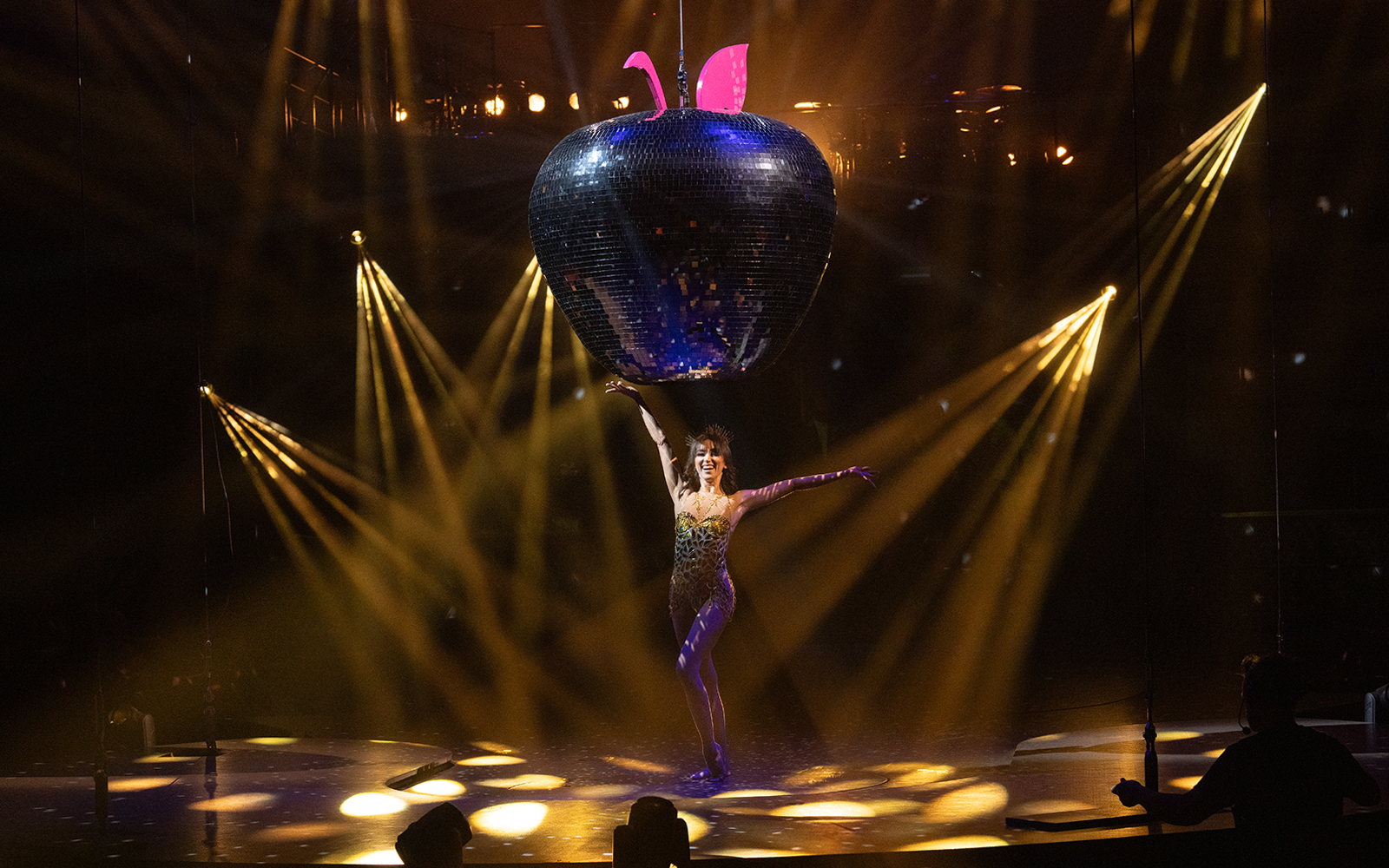 Performer on stage with large disco apple prop in Mad Apple show.