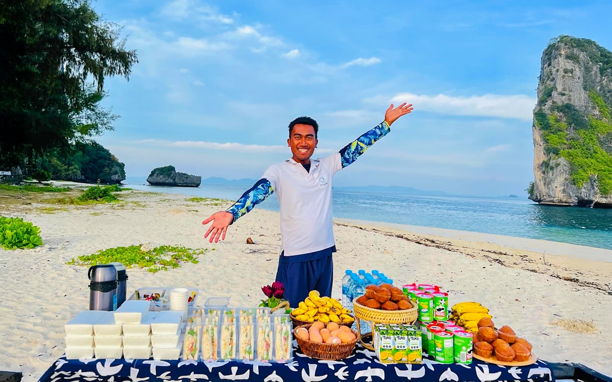 Buffet lunch setup on Phi Phi Don beach with a smiling host and scenic ocean view.