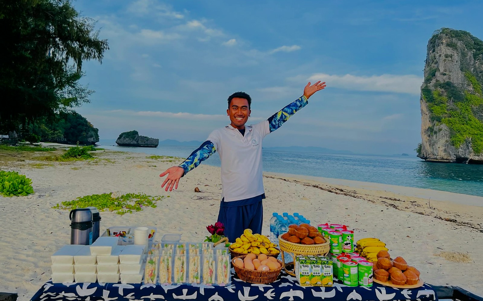 Buffet lunch setup on Phi Phi Don beach with a smiling host and scenic ocean view.