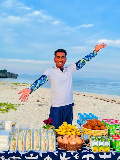 Buffet lunch setup on Phi Phi Don beach with a smiling host and scenic ocean view.