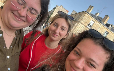 Three people smiling in front of historic buildings during Bordeaux Murder Mystery city exploration game.