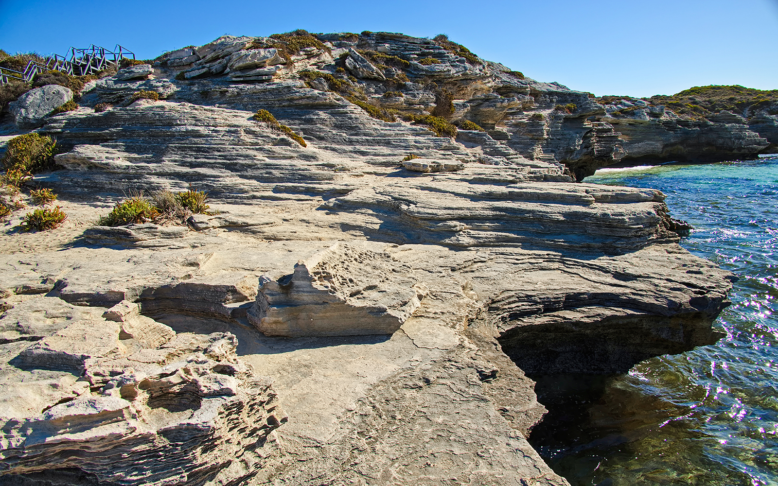 Rocky shoreline at Henrietta Rocks, Rottnest Island, with clear blue water and rugged cliffs.